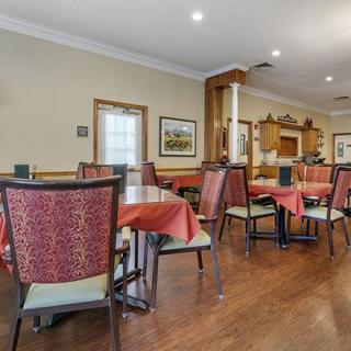 A cozy dining area with neatly arranged tables and chairs, featuring warm decor and wood flooring.