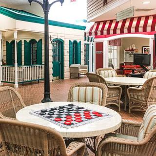 An inviting indoor space with tables and chairs, featuring a checkerboard for games, surrounded by decorative storefronts.