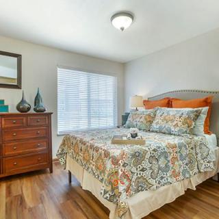 A cozy bedroom with a patterned bedspread, wooden dresser, and natural light filtering through the window.