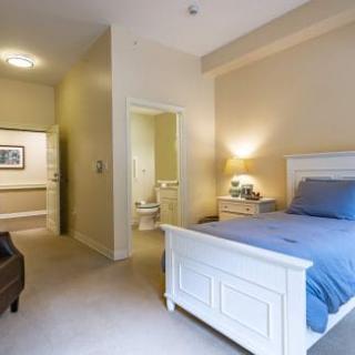 A cozy bedroom featuring a white bed with blue bedding, a bedside lamp, and an en-suite bathroom.