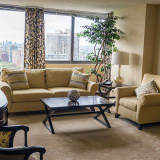 A cozy living room with a sofa, armchair, and coffee table, featuring a large window with a city view.