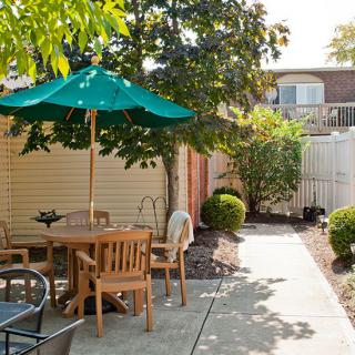A sunny backyard with outdoor seating and a green umbrella, surrounded by plants.
