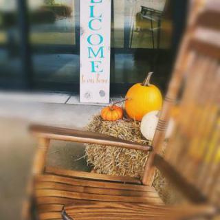 A cozy autumn welcome setup featuring pumpkins and a rustic chair.
