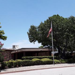 A view of a building with an American flag and well-maintained landscaping under a clear blue sky.