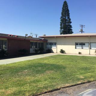 A small, single-story building with a well-maintained lawn and a tall tree in the background under a clear blue sky.