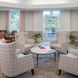 A cozy living room setup with armchairs around a coffee table, plants, and ample natural light from large windows.
