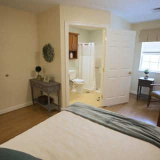A cozy bedroom with an adjacent bathroom, featuring natural light and simple decor.