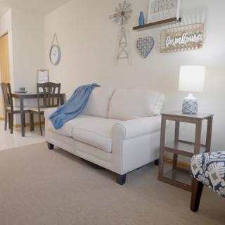 A cozy living room with a white sofa, wall decorations, and a small dining area in the background.