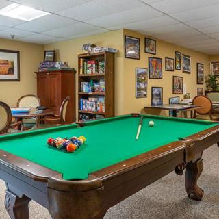 A cozy game room featuring a pool table with green felt, surrounded by framed pictures and a bookcase.
