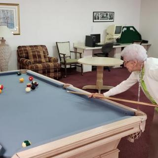An elderly woman playing pool in a recreation room.