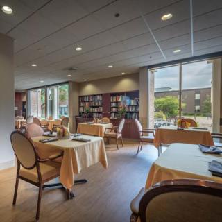 A cozy library reading area with tables and chairs near large windows.
