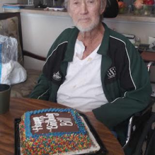 An elderly man sitting in a wheelchair with a colorful birthday cake.