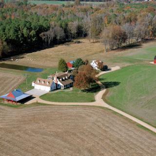 An aerial view of a tranquil rural farm surrounded by fields and autumn foliage.