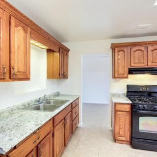 A kitchen with wooden cabinets, granite countertops, a stove, and a sink.