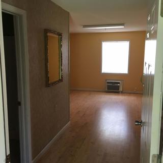 A view of an empty room with wooden flooring and a window.