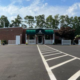 A commercial building featuring a green awning, surrounded by trees under a partly cloudy sky.