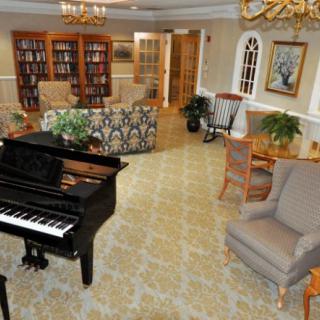 A cozy lounge area featuring a grand piano, comfortable seating, and bookshelves filled with books.