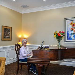 A person playing a grand piano in a warmly lit living room, adorned with flowers and artwork.