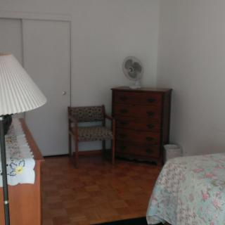 A minimalist bedroom with essential furniture including a lamp, dresser, chair, and bed.