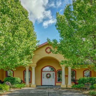 A charming house entrance with an archway and columns, flanked by lush green trees on a sunny day.