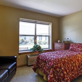 A cozy bedroom with a single bed, wooden dresser, and large window bringing in natural light.