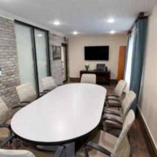 A modern conference room with a large table and chairs, featuring a TV on the wall.