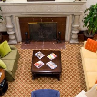 A cozy living room with a fireplace, featuring colorful couches and a central coffee table with magazines.