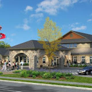 A scenic view of a modern building with stone accents, surrounded by landscaping, and a parking lot with cars and people nearby.