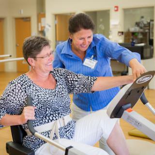 A physical therapist assists an older woman during a workout session, promoting health and fitness.