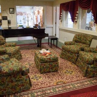 A cozy living room featuring patterned armchairs, a piano, and an ornate carpet.
