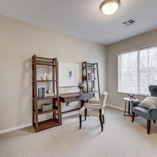A cozy home office with a wooden desk, bookshelves, and a comfortable chair by the window.
