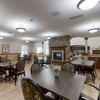 A well-lit dining room with multiple tables and chairs, featuring a central fireplace.