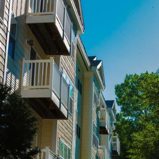 A residential apartment building with balconies against a clear blue sky and surrounded by trees.