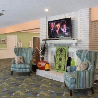 A cozy living room with a white brick fireplace, television, and comfortable striped chairs.