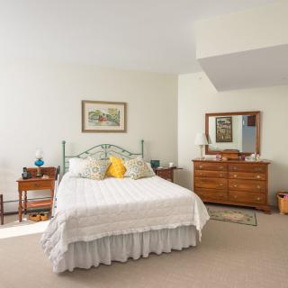 A cozy bedroom featuring a bed with decorative pillows, wooden dressers, and a large mirror.