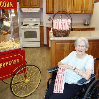 An elderly person in a wheelchair enjoying popcorn in a kitchen setting.