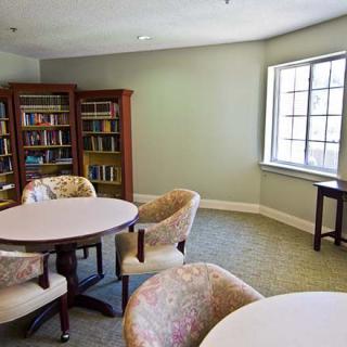 A quiet library reading area with tables, chairs, and bookshelves by a window.