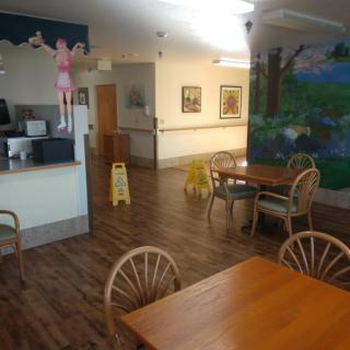 A cozy dining area with wooden floors, tables, chairs, and a colorful mural on the wall.