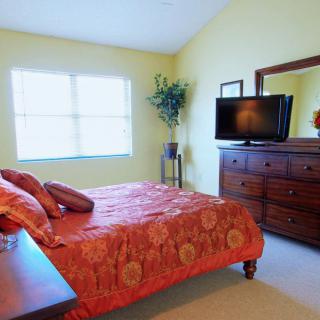 A cozy bedroom with orange bedding and a wooden dresser, featuring a television and window.