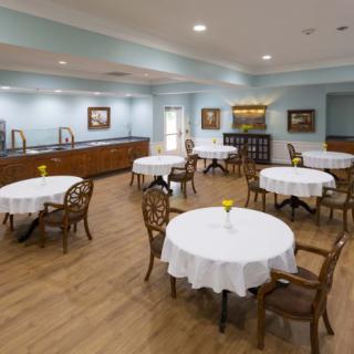 A well-lit dining room with round tables and wooden chairs, featuring elegant decor.