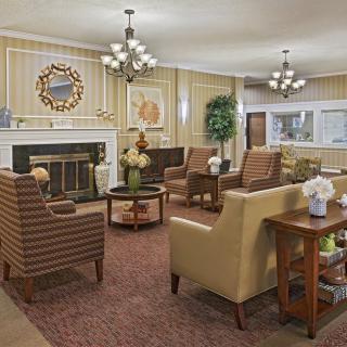 A cozy, elegantly decorated living room with armchairs, a sofa, a fireplace, and chandeliers.
