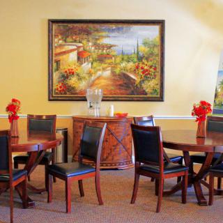 A cozy dining area with round tables and chairs, adorned with a landscape painting on the wall.