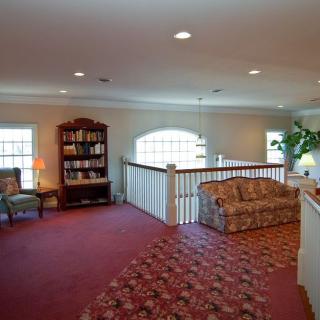 A cozy living area with a red carpet, comfortable sofa, bookshelf, and soft lighting.