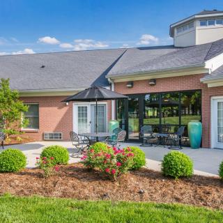 A brick building with a patio and landscaped garden area featuring outdoor seating and greenery.