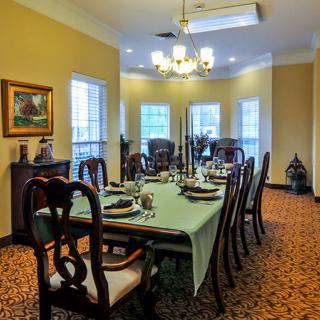 A formal dining room with a long table set for a meal, featuring elegant chairs and a chandelier.