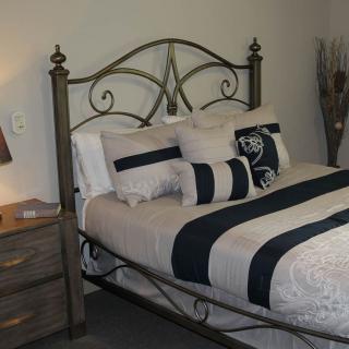 A cozy bedroom with a decorative metal headboard, patterned bedding, and a bedside lamp.