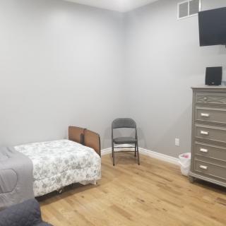A minimalist bedroom featuring a single bed, chair, dresser, and a wall-mounted television.