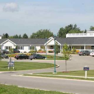 A view of a large building with a parking lot and cars in front, surrounded by trees and a well-maintained lawn.