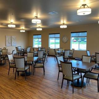An empty dining room with neatly arranged tables and chairs, featuring large windows and overhead lighting.