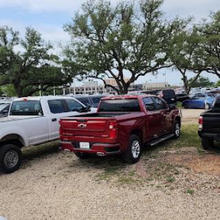 A red pickup truck parked among other vehicles in a grassy area with trees.